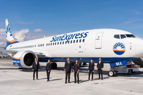 A SunExpress airplane at an airport gate, with the six flight crew standing on the ground outside